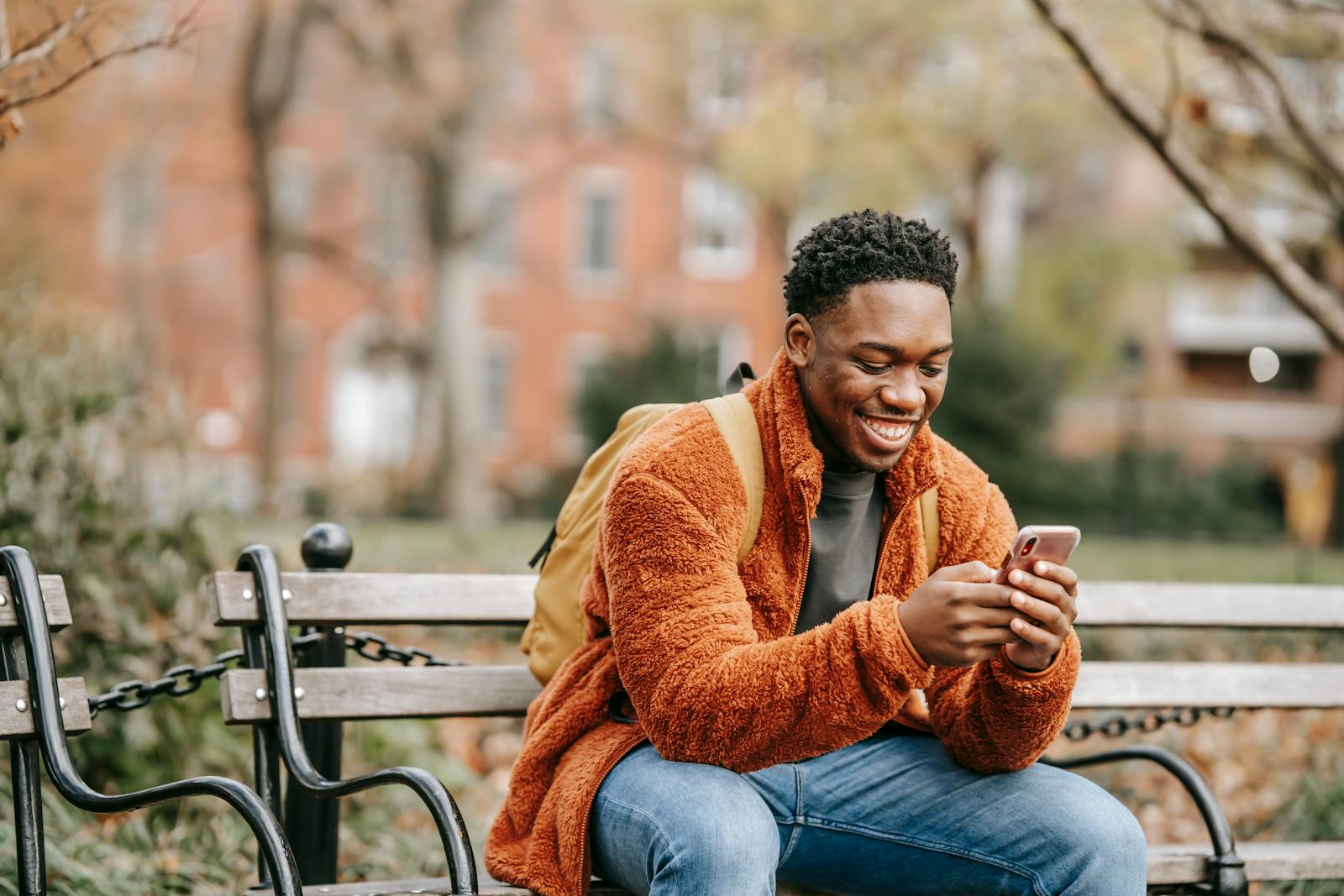 Delightful African American man surfing modern cellphone in city park